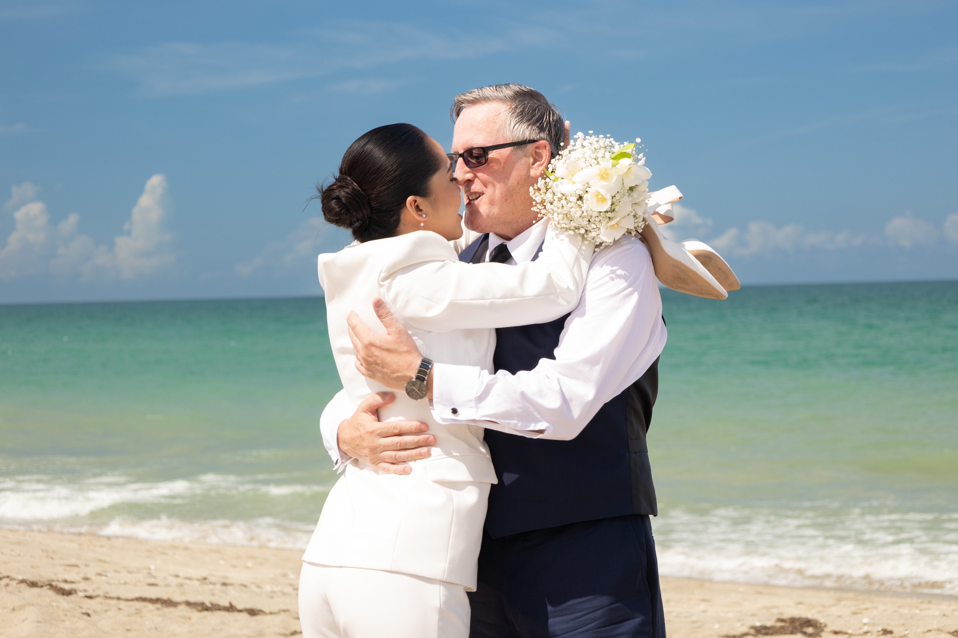 Bride and groom embracing on the beach with turquoise water behind them