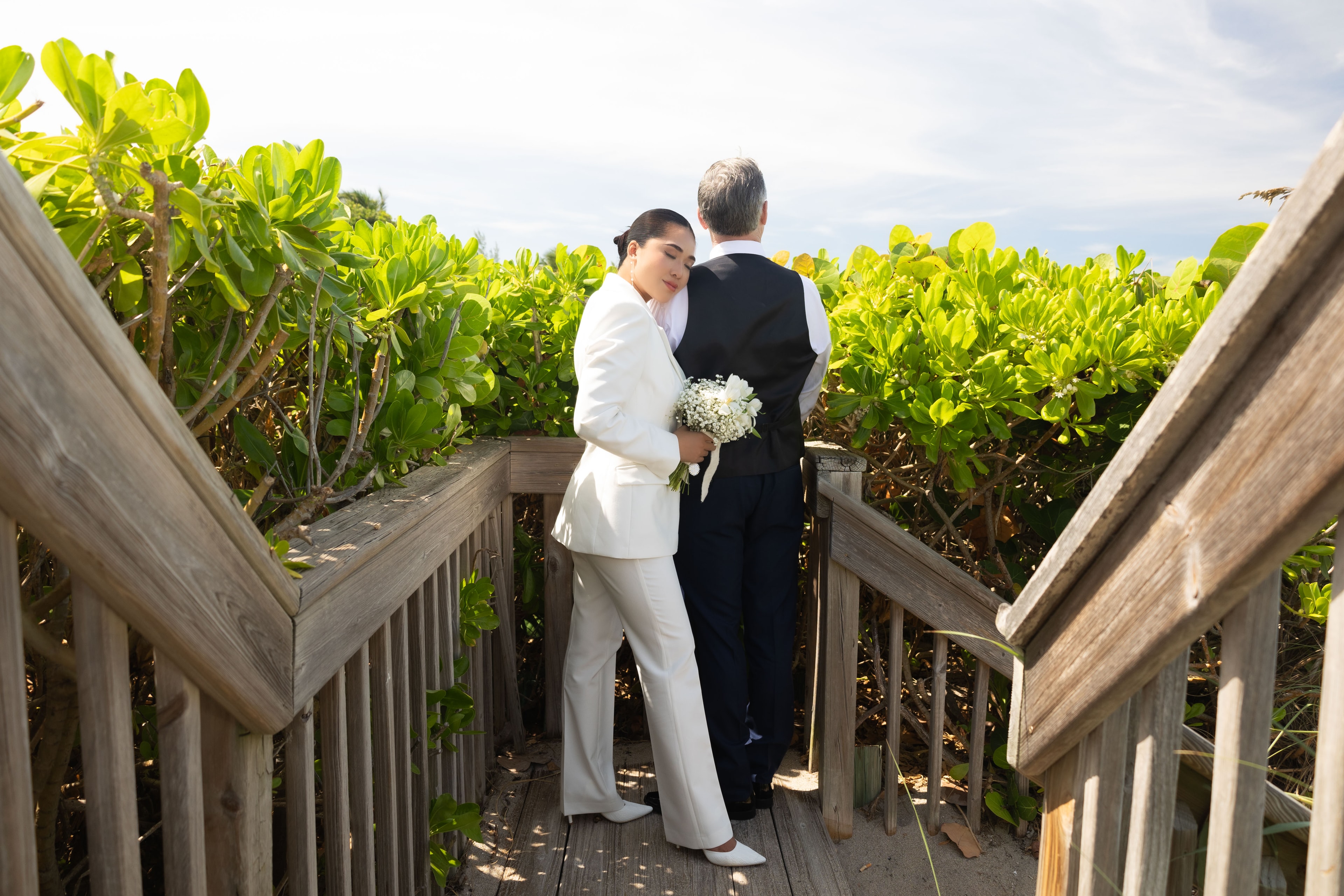 Couple standing together on beach boardwalk surrounded by lush foliage