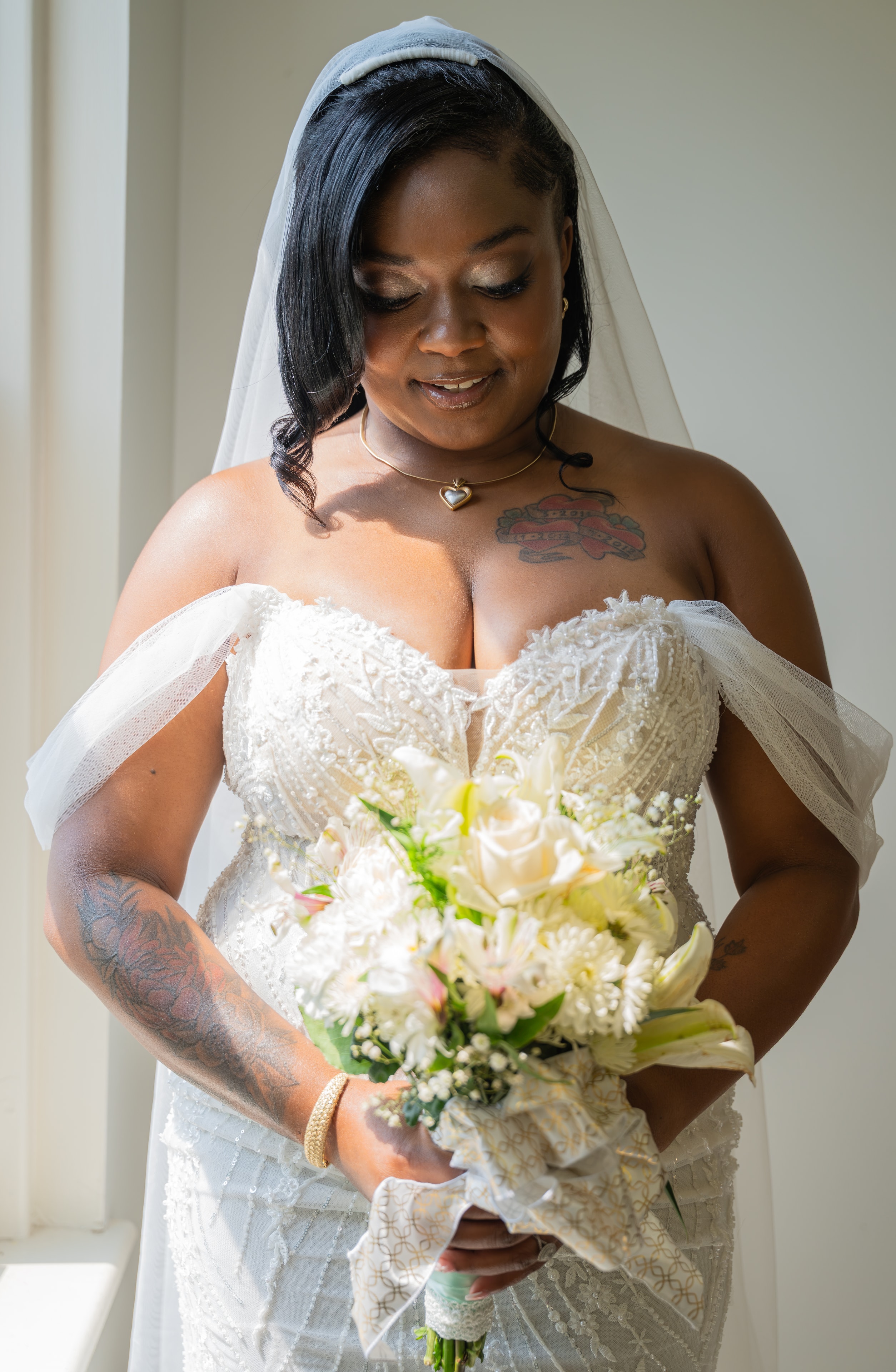 Bride looking down at bouquet in window light