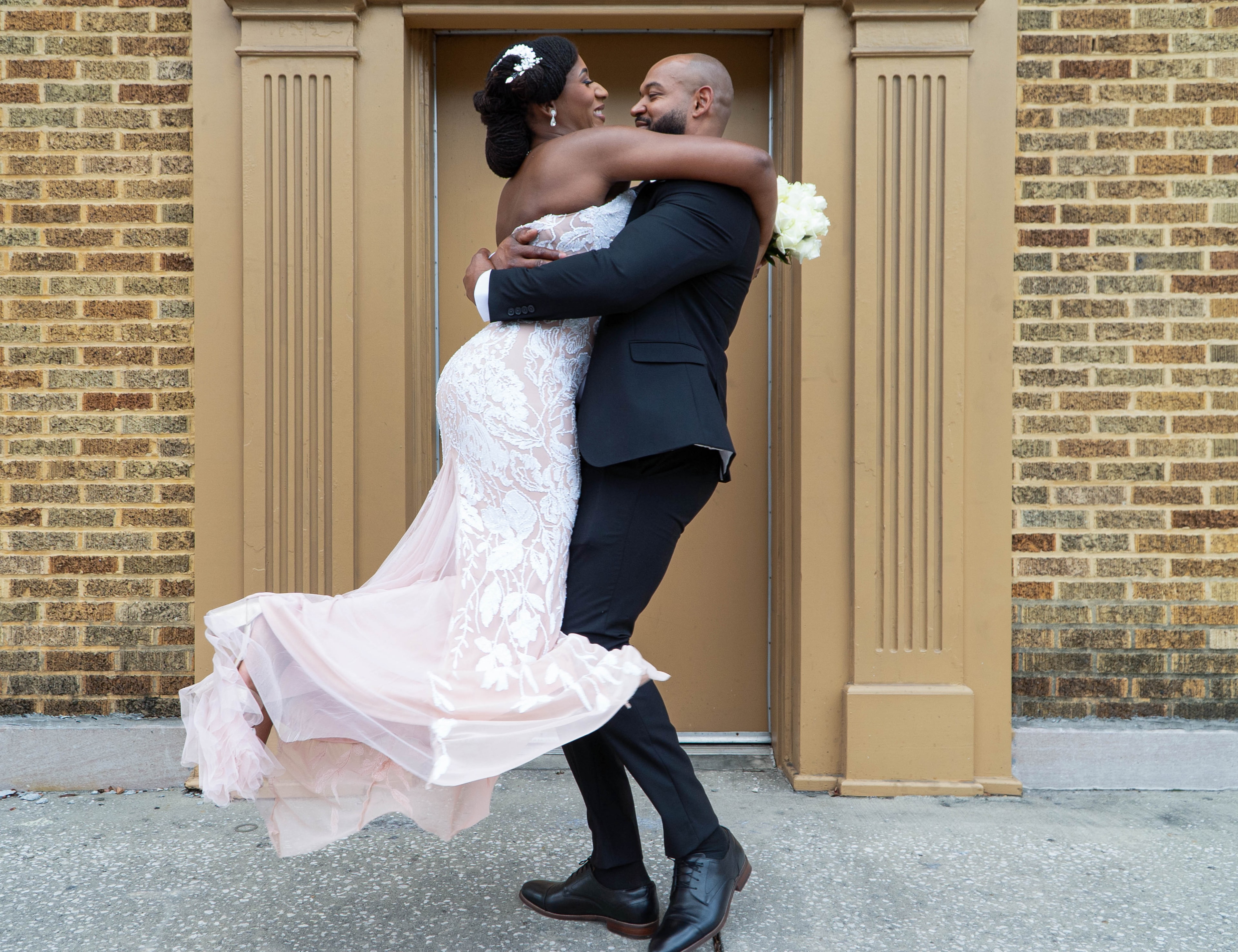 Groom lifting bride in front of brick building